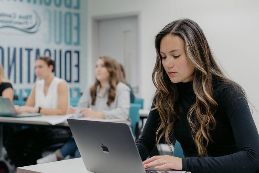 Students take notes on laptops during a lecture in a classroom.